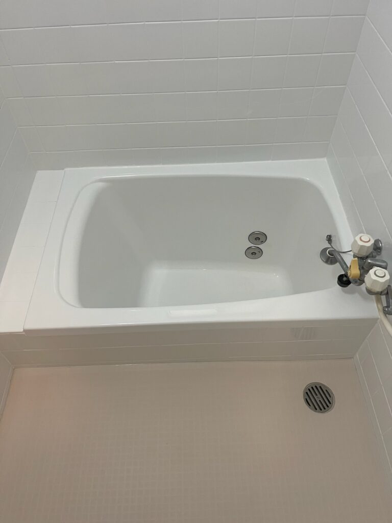 塗装仕上げの白い浴槽と壁、床に施工されたアイボリーのバスナフローレが明るさを演出する浴室